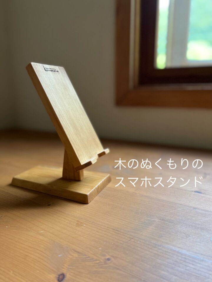 窓際の机の上の木製スマホスタンド　斜め