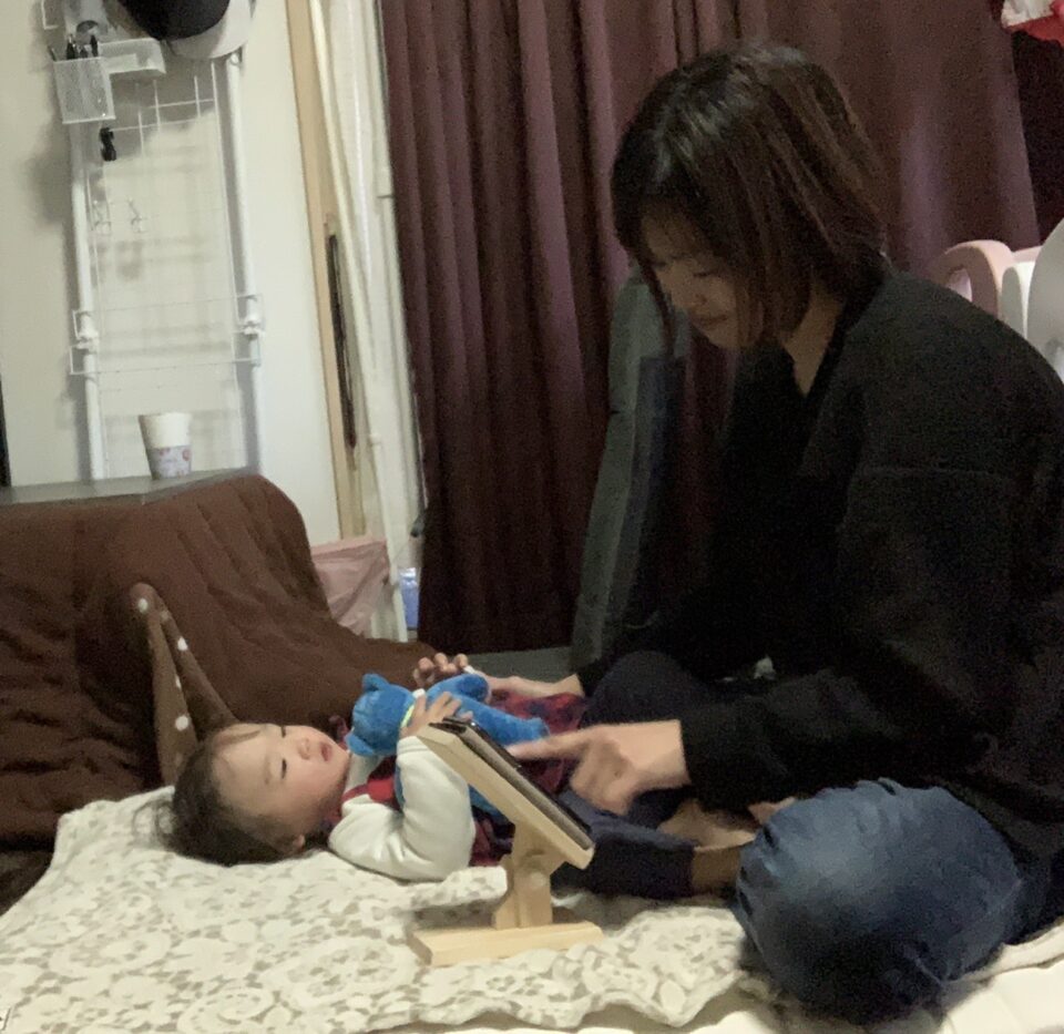 ママが赤ちゃんを寝かしつけながら木製スマホスタンドのスマホ操作