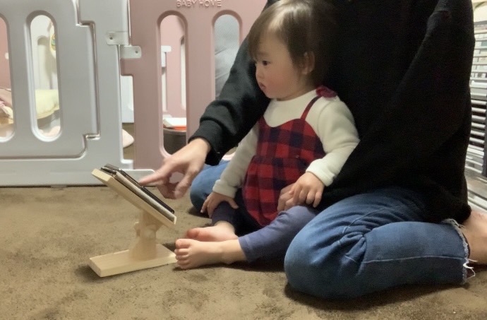 ママの膝で赤ちゃんが一緒に木製スマホスタンドのスマホを操作。