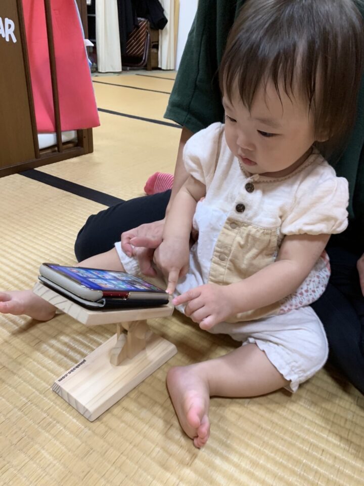 ママの膝で赤ちゃんが一緒に木製スマホスタンドのスマホを操作。