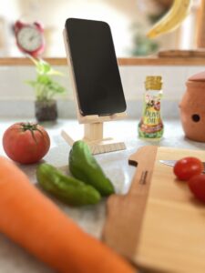 キッチンで野菜達と木製スマホスタンドにiphoneが載っている